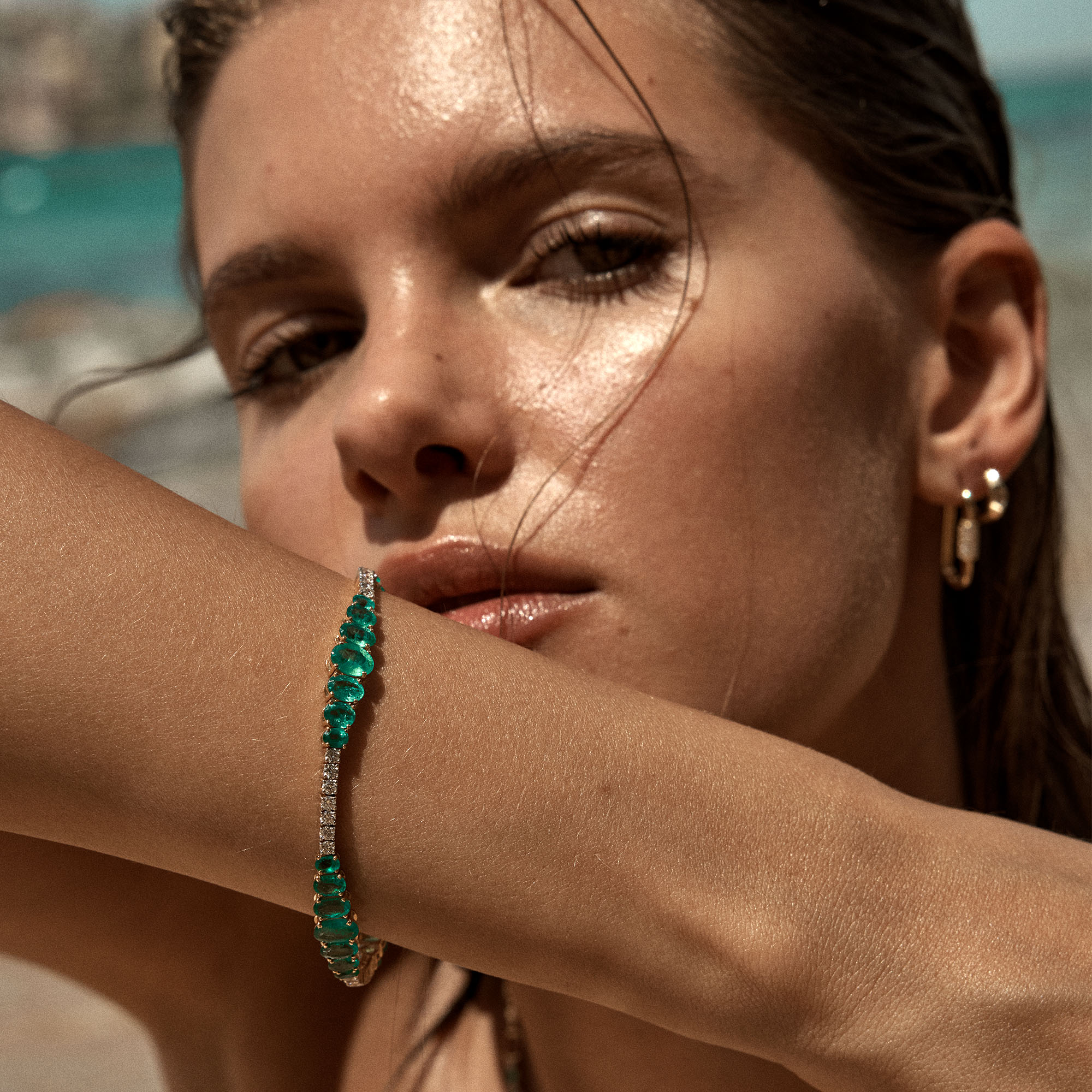 Woman wearing 8.63 carat Zambian emerald and 1.50 carat diamond tennis bracelet in 18-karat yellow gold on sun-drenched skin, Odyssey Collection luxury jewelry by Astrid Montague Australia