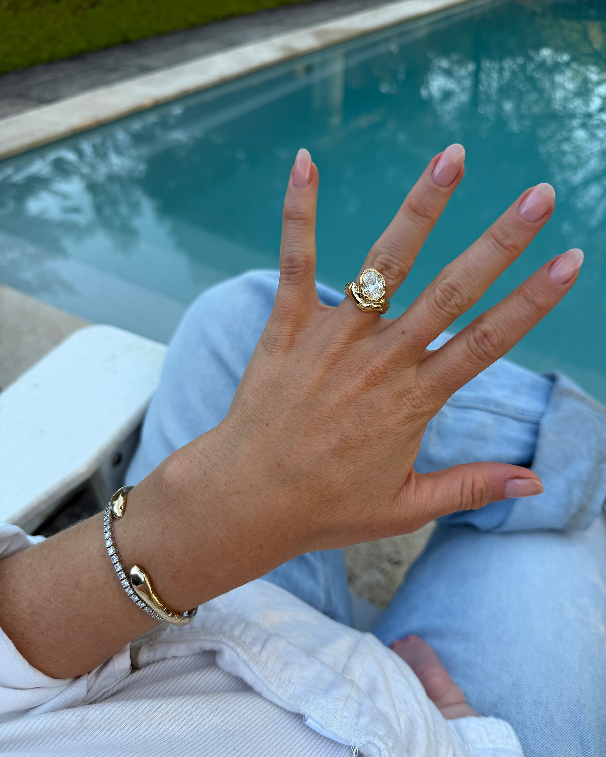 Oyster Heirloom diamond ring in sculptural 18ct yellow gold, worn on a hand beside a turquoise swimming pool